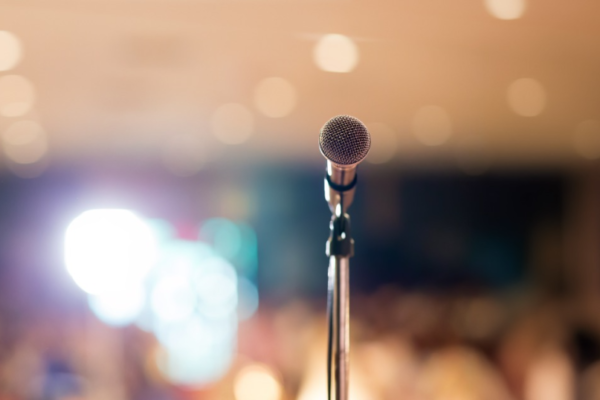 “A microphone on a stand against a softly blurred, warmly lit event venue.